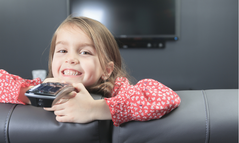 niña pequeña con control remoto delante de un televisor.