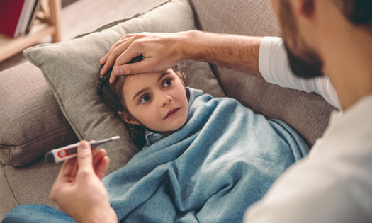 Sick little girl covered in blanket is lying on couch while her father is taking her temperature