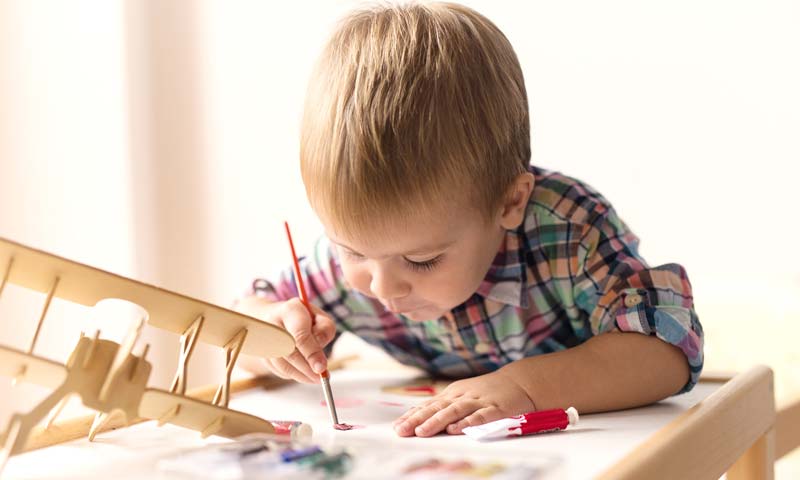 Niño pintando su avión de madera solo