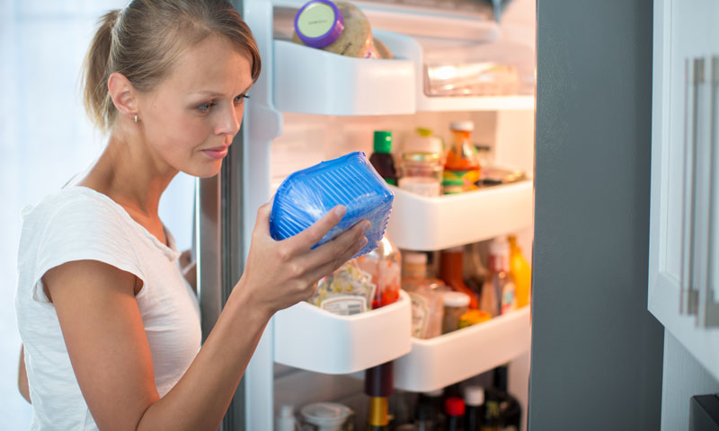 Madre comprobando la fecha de caducidad del paquete de comida del frigorífico