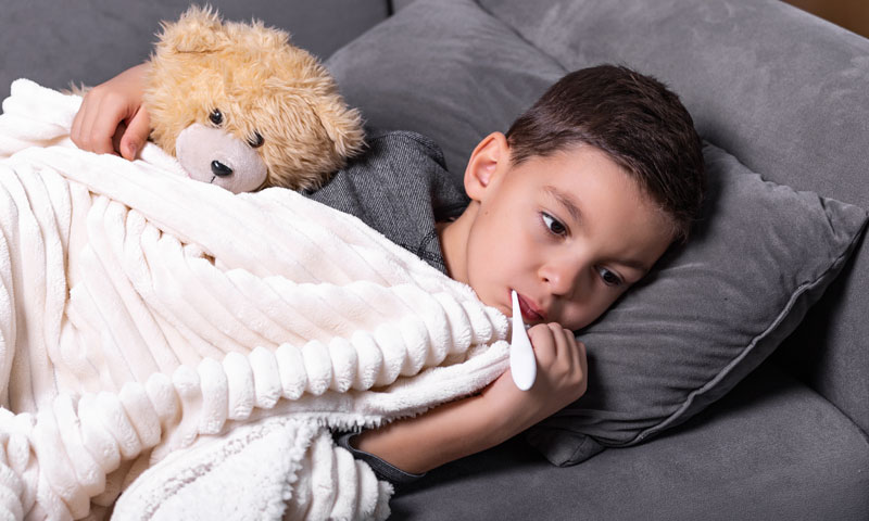 Niña pequeña enferma con gripe en la cama mientras el padre le toma la temperatura con un termómetro y le toca la frente con la mano