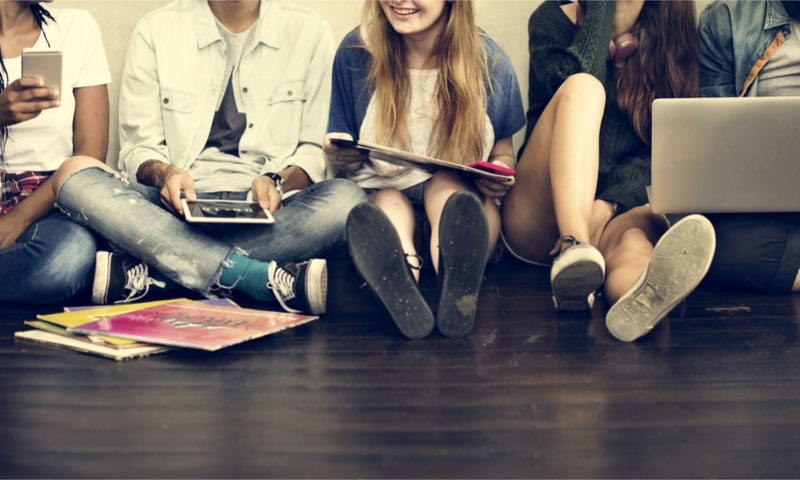 un grupo de adolescentes sentados en el suelo utilizando sus dispositivos electrónicos