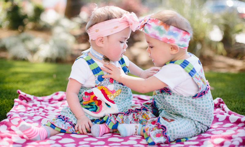 Las mellizas Cora y Farrah sentadas en una manta de picnic al aire libre