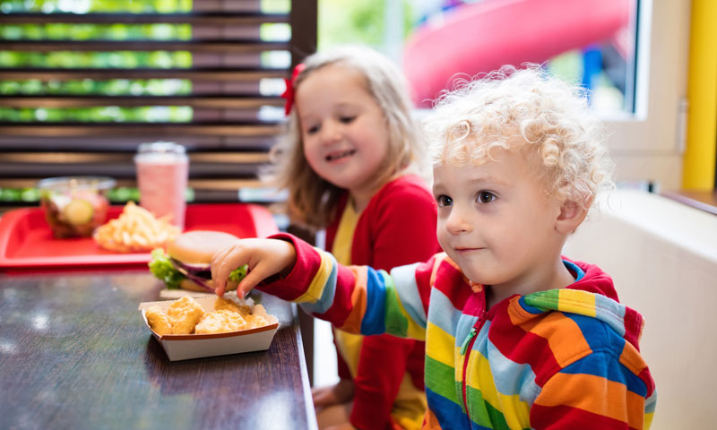 Niños pequeños comiendo patitas de pollo de comida rápida