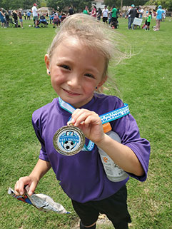 Niña pequeña sosteniendo su medalla mientras sonríe