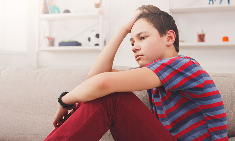 Niño adolescente sentado sosteniendo su cabeza