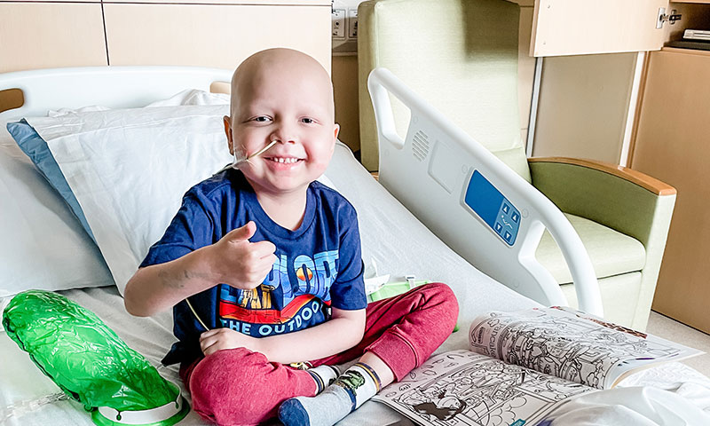 Little boy in a hospital bed smiling with a coloring book.