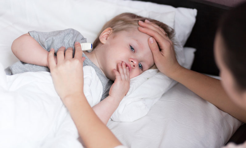 Madre tomando la temperatura del hijo enfermo mientras está tumbado en la cama