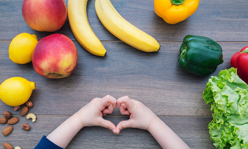Manos formando un corazón mientras muestran frutas y verduras