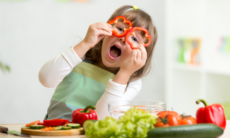 niña divirtiéndose con alimentos y vegetales en la cocina