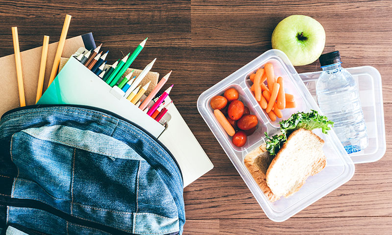 mochila con útiles escolares junto a un almuerzo nutritivo