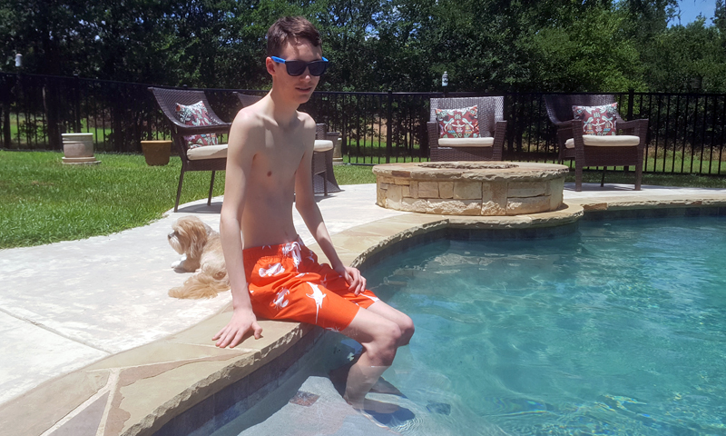 John sentado al borde de la piscina con los pies en el agua
