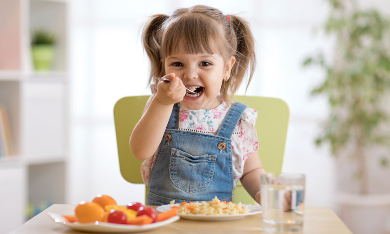 Niña pequeña comiendo alimentos saludables en la mesa
