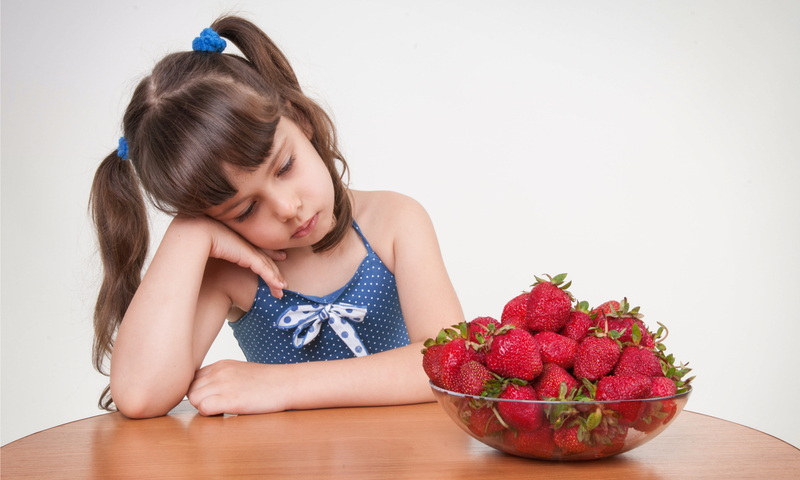 Niña pequeña sentada en una mesa mirando un tazón de fresas