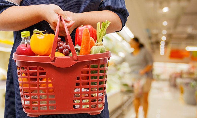 mujer sosteniendo la cesta de la compra llena de alimentos saludables