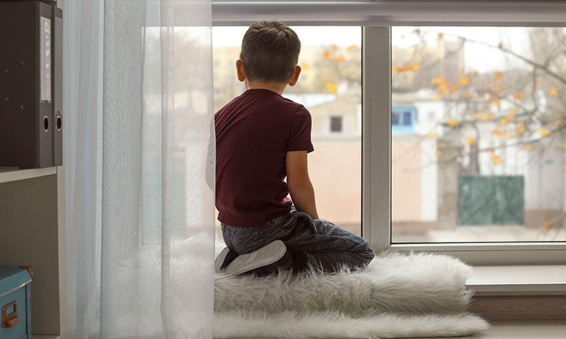 niño sentado junto a la ventana mirando hacia afuera