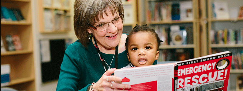 La bibliotecaria Carol Miller con el paciente David leyendo en la biblioteca de Children's Health.