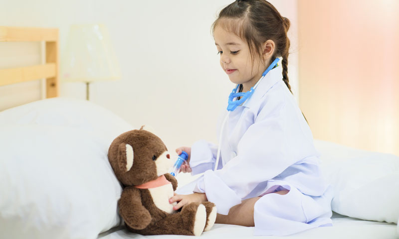 Niña pequeña jugando al doctor dándole una vacuna a su osito de juguete