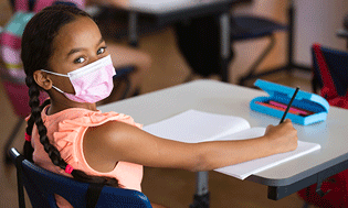 Niña en un aula con una mascarilla rosa - Children's Health