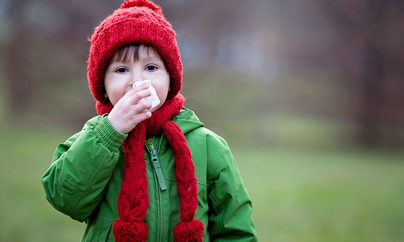 Niño al aire libre soplándose la nariz el día de invierno