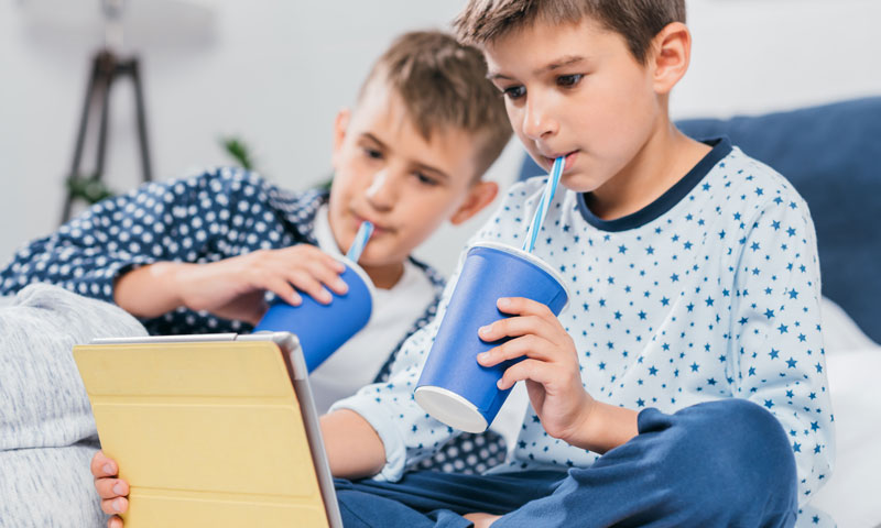 dos niños pequeños viendo videos en una tableta bebiendo refrescos