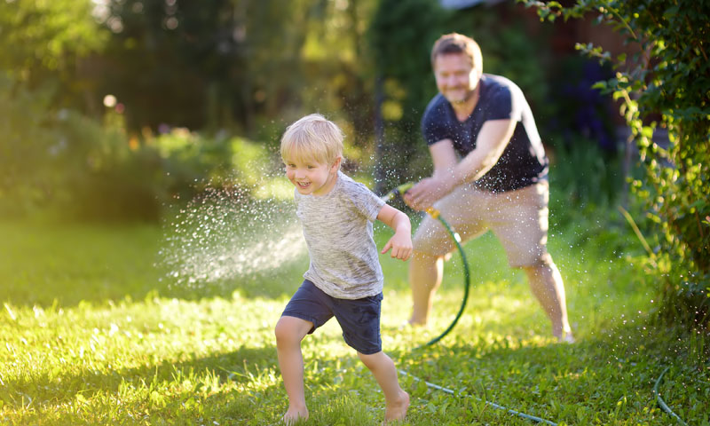 Niño pequeño jugando en el patio con manguera de agua con su padre