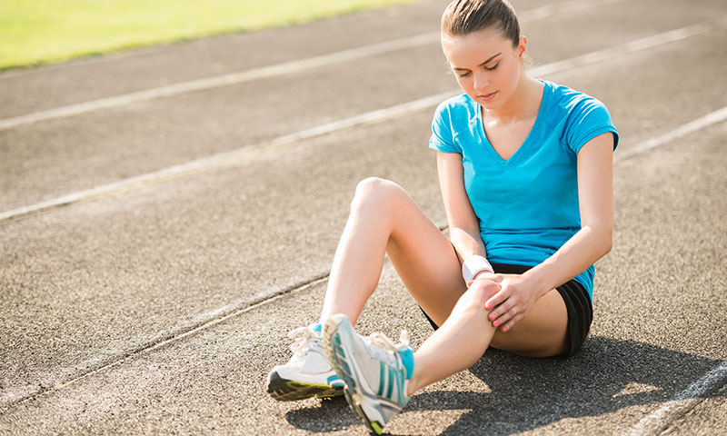 Chica adolescente sentada en una pista de atletismo sujetando la rodilla