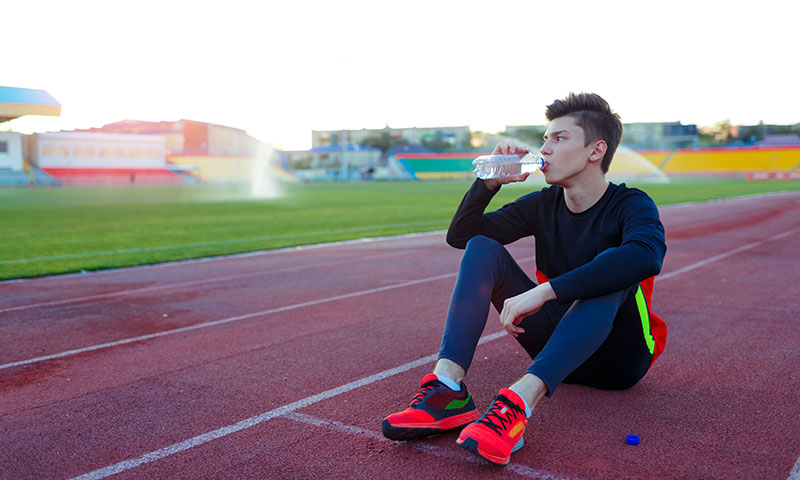 Atleta adolescente bebiendo agua en la pista de atletismo