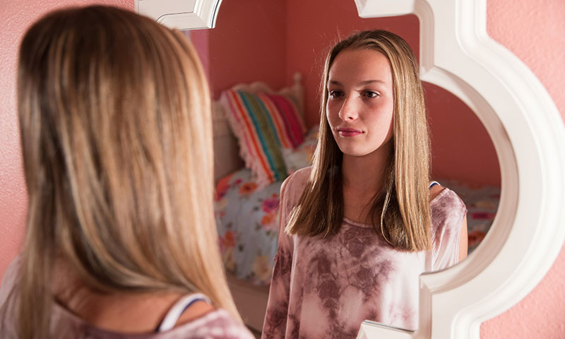 Chica adolescente que se mira a sí misma en el espejo