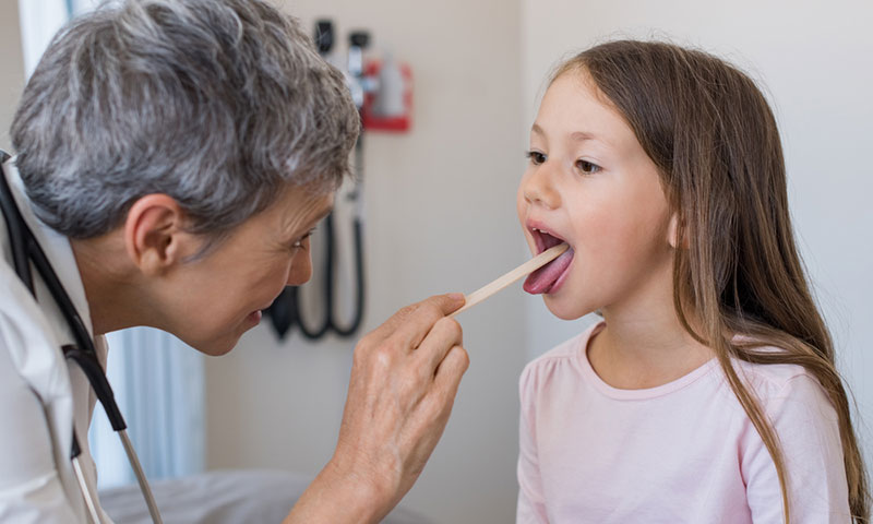 Médica examinando la garganta de una niña pequeña