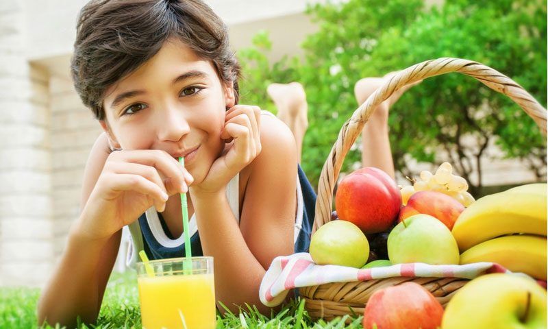 Adolescente tumbado en un campo de césped verde fresco y bebiendo un delicioso jugo, comiendo frutas, disfrutando de una nutrición saludable en un día de verano
